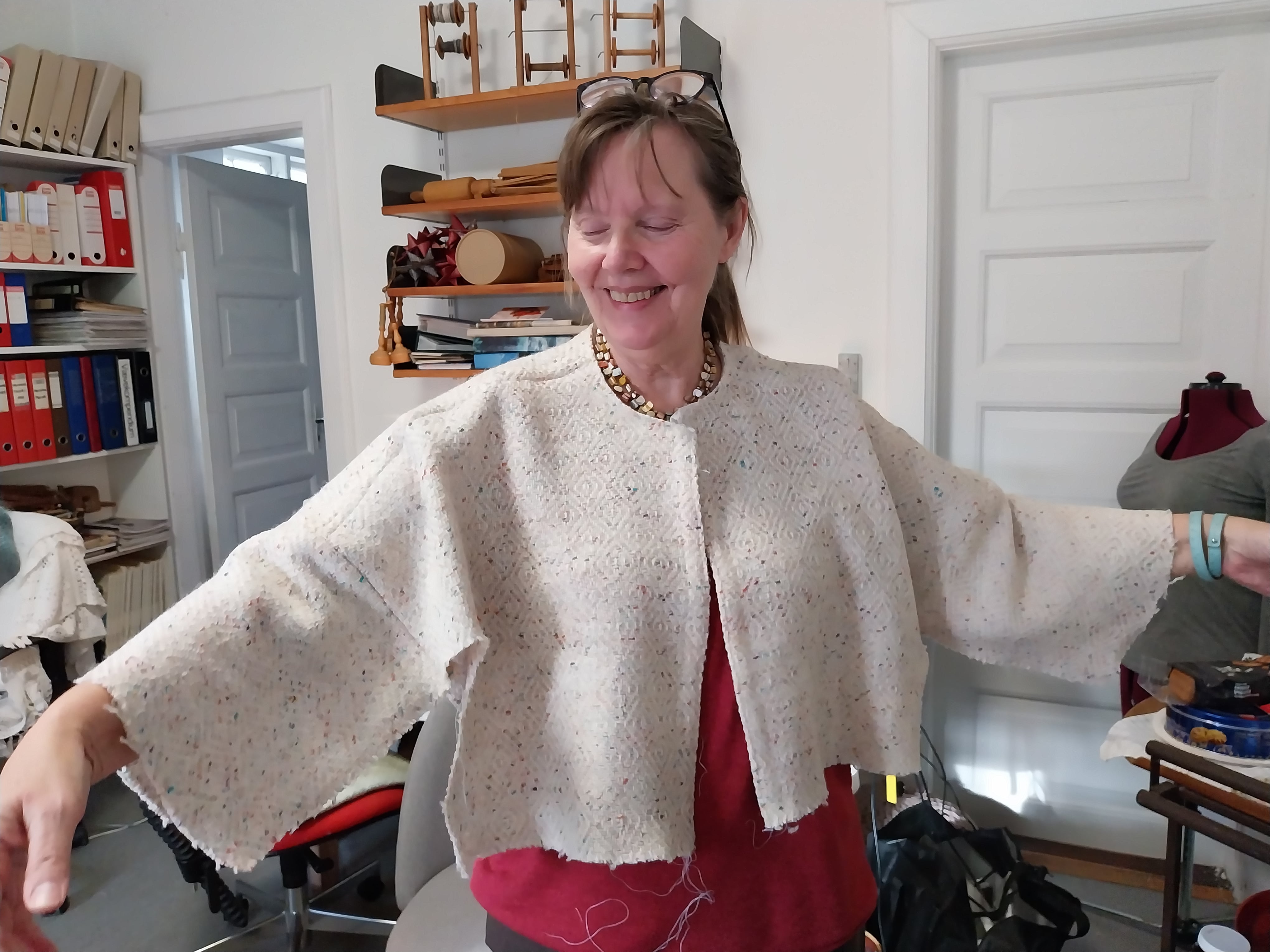 Lone Ø har klippet sit vævede stof, og er ved at prøve (pas på, hun stritter af knappenåle)